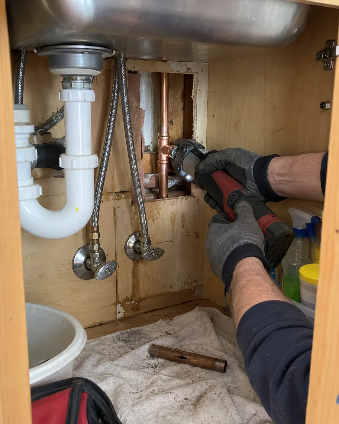 Professional plumber repairing a burst copper water pipe beneath a kitchen sink in Ottawa